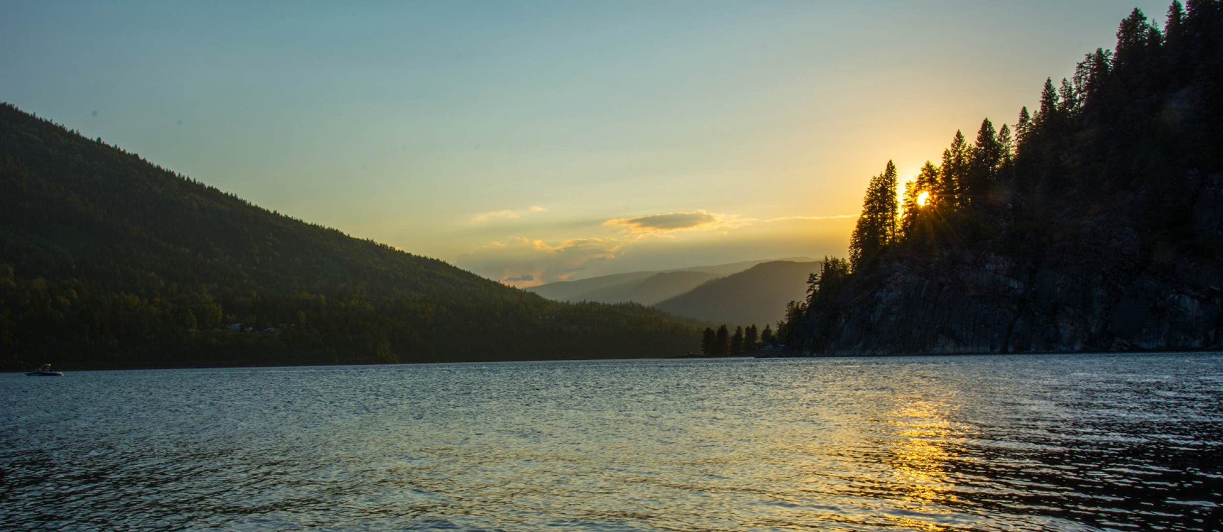 The sun setting behind trees on the shore of Kootenay Lake