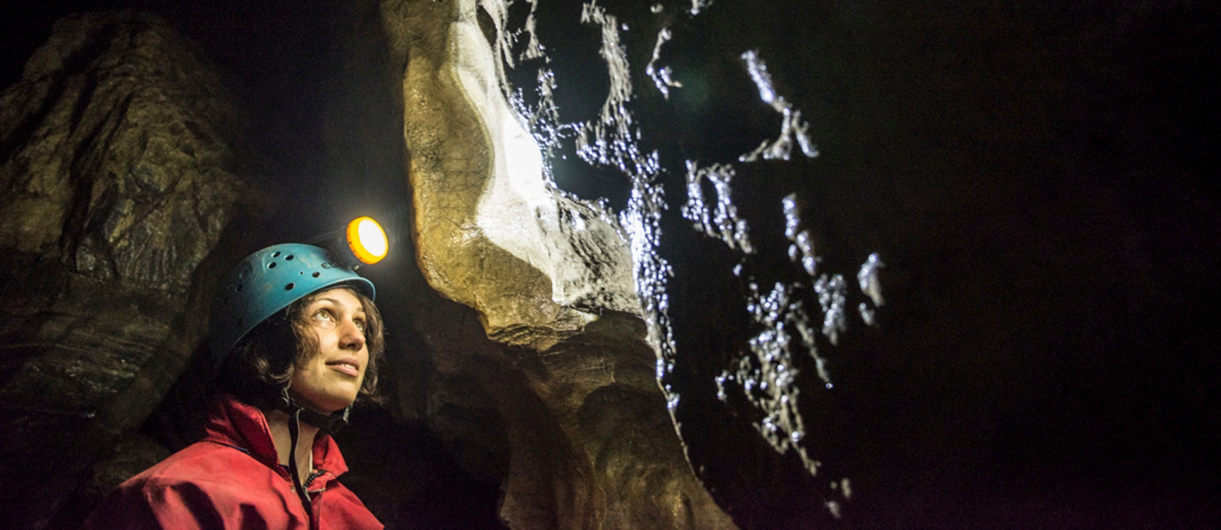 A person with a helmet and headlamp on looking up at a wall inside Cody Caves, near Nelson BC