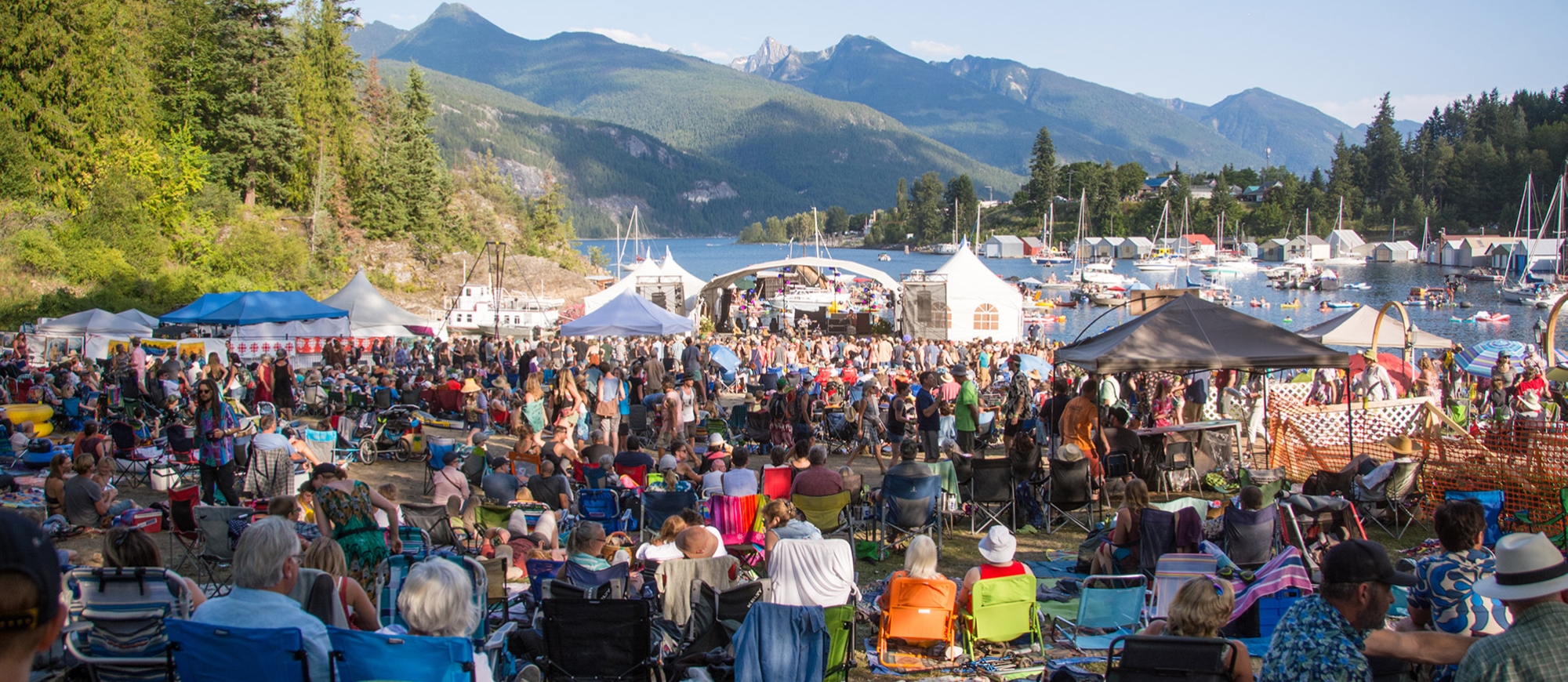People sitting on the grass looking towards the floating stage on a sunny day at kaslo jazz festival
