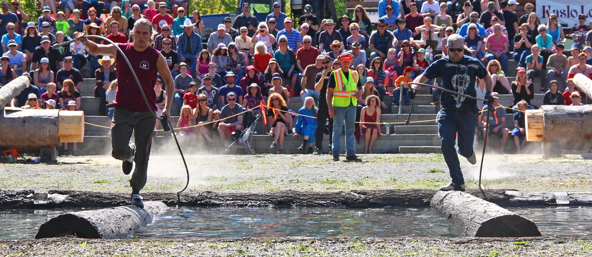 Two men running on a log in water during Kaslo Logger Sports at May Days in Kaslo, BC.