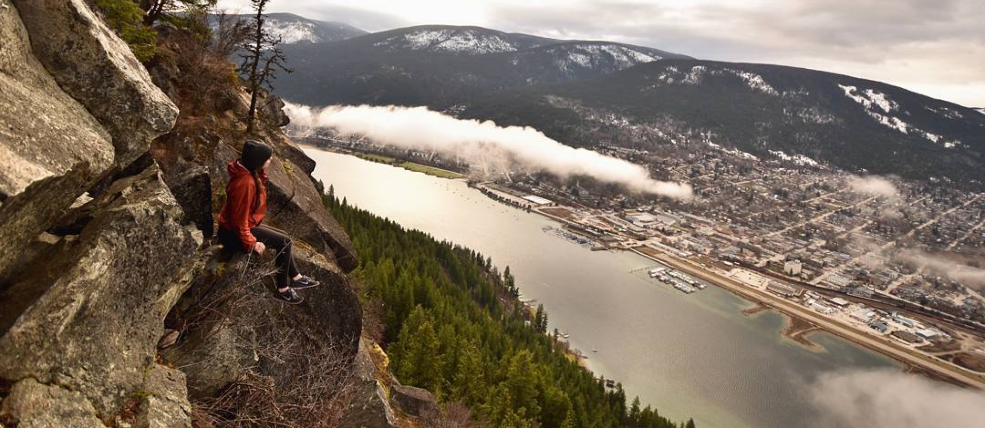 A woman sitting on pulpit rock, looking down on Nelson BC far below