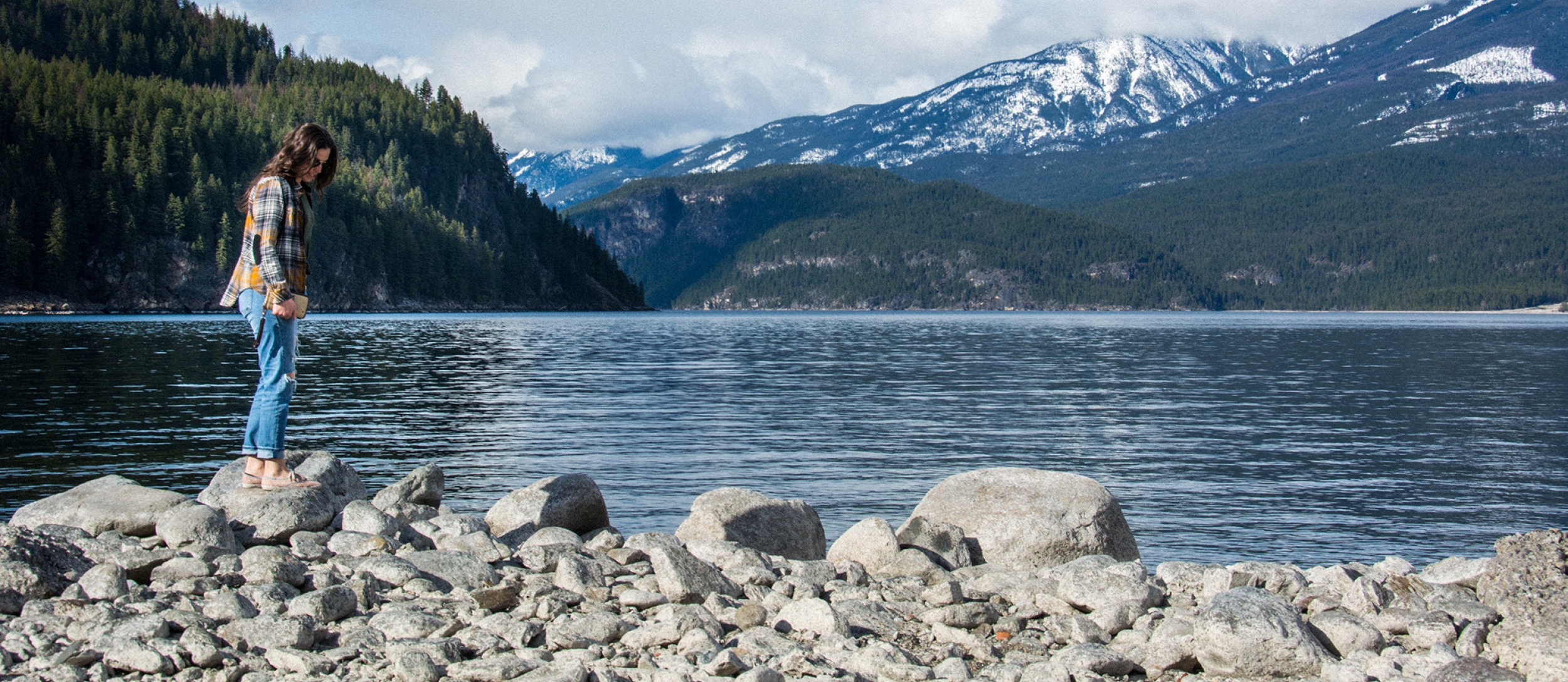 A girl standing on a rock on the beach in Kaslo, BC