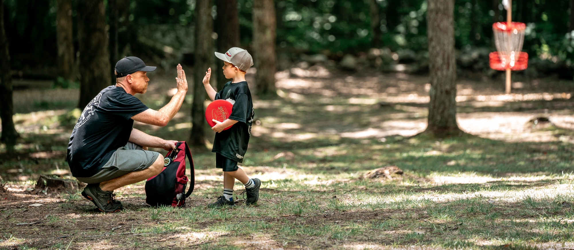 Man giving a high 5 to a small child at a disc golf course