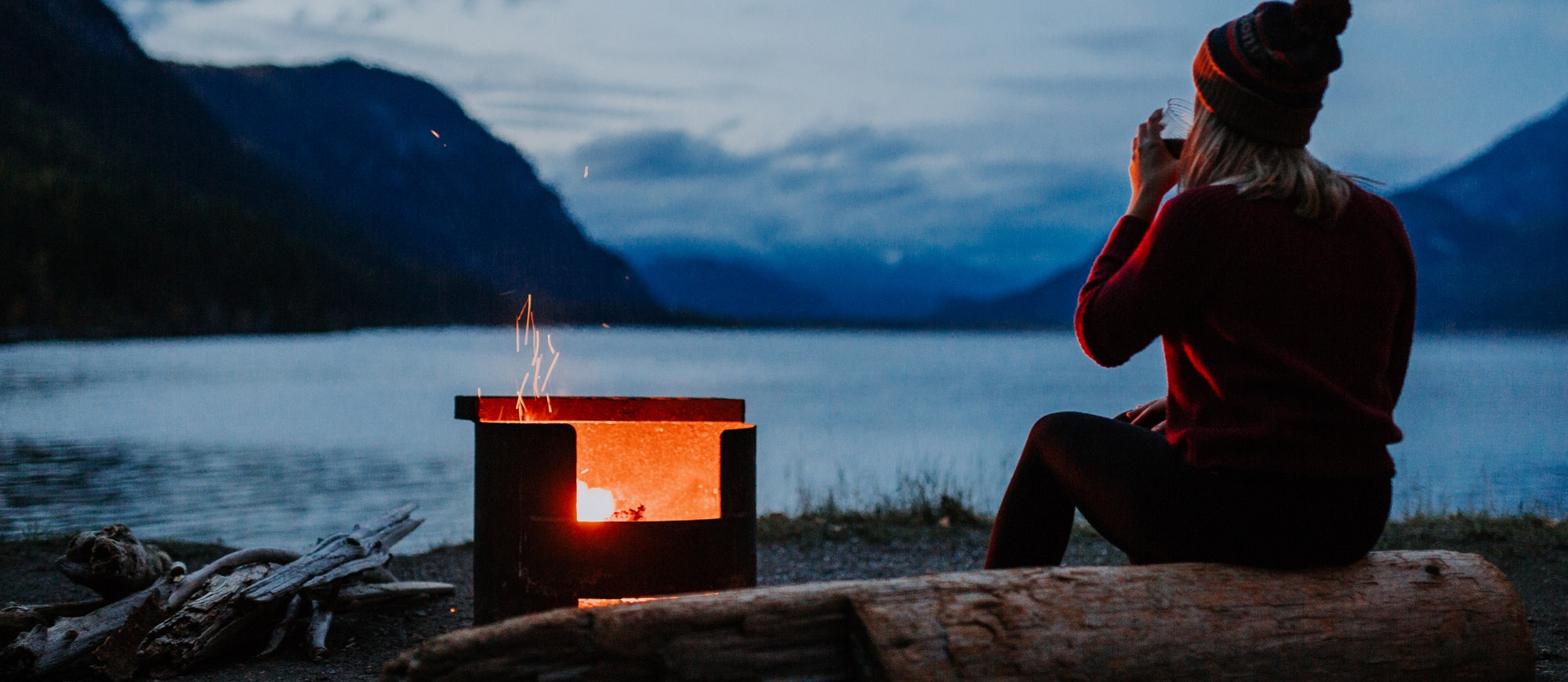 A girl sitting by a campfire on the shores of Kootenay Lake, BC.