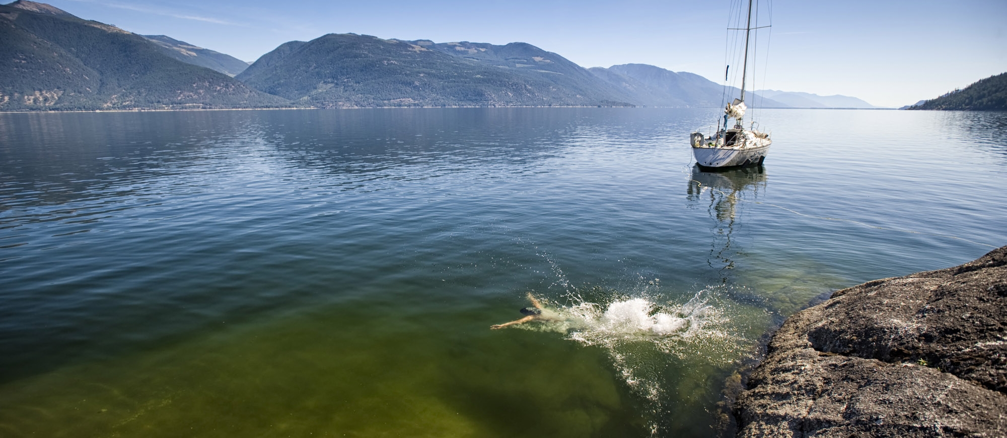 Jumping into Kootenay Lake with a sailboat in the background. 
