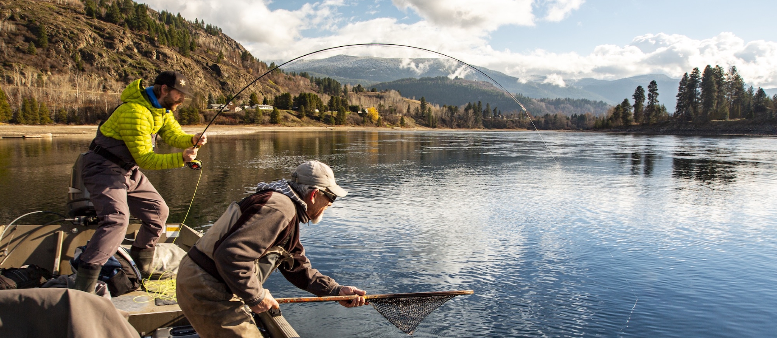 A man has a fish on his line, the other man has a net ready for him on the Columbia River with Reel Adventures