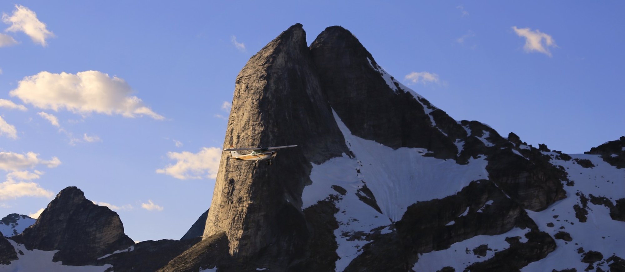 A Kootenay Lake Aviation plane flies near a large mountain