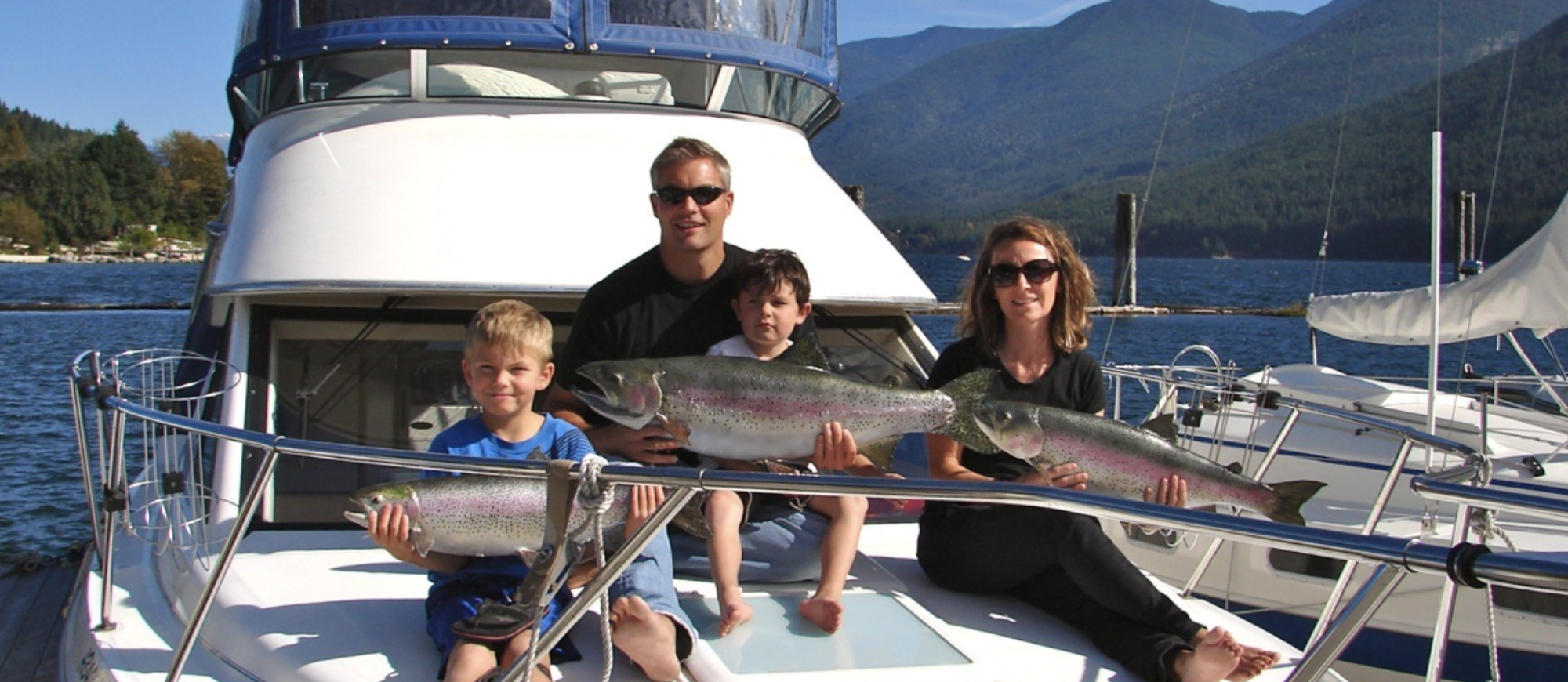A mom, dad and two children hold up the fish they've caught on a Kootenay Wild Fishing Charter boat