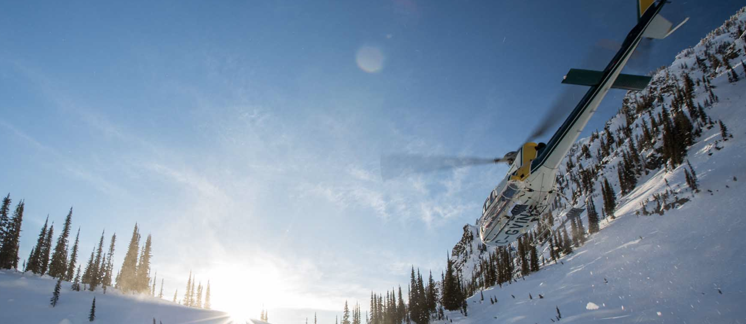 photo of a high terrain helicopter landing in the snow surrounded by mountains