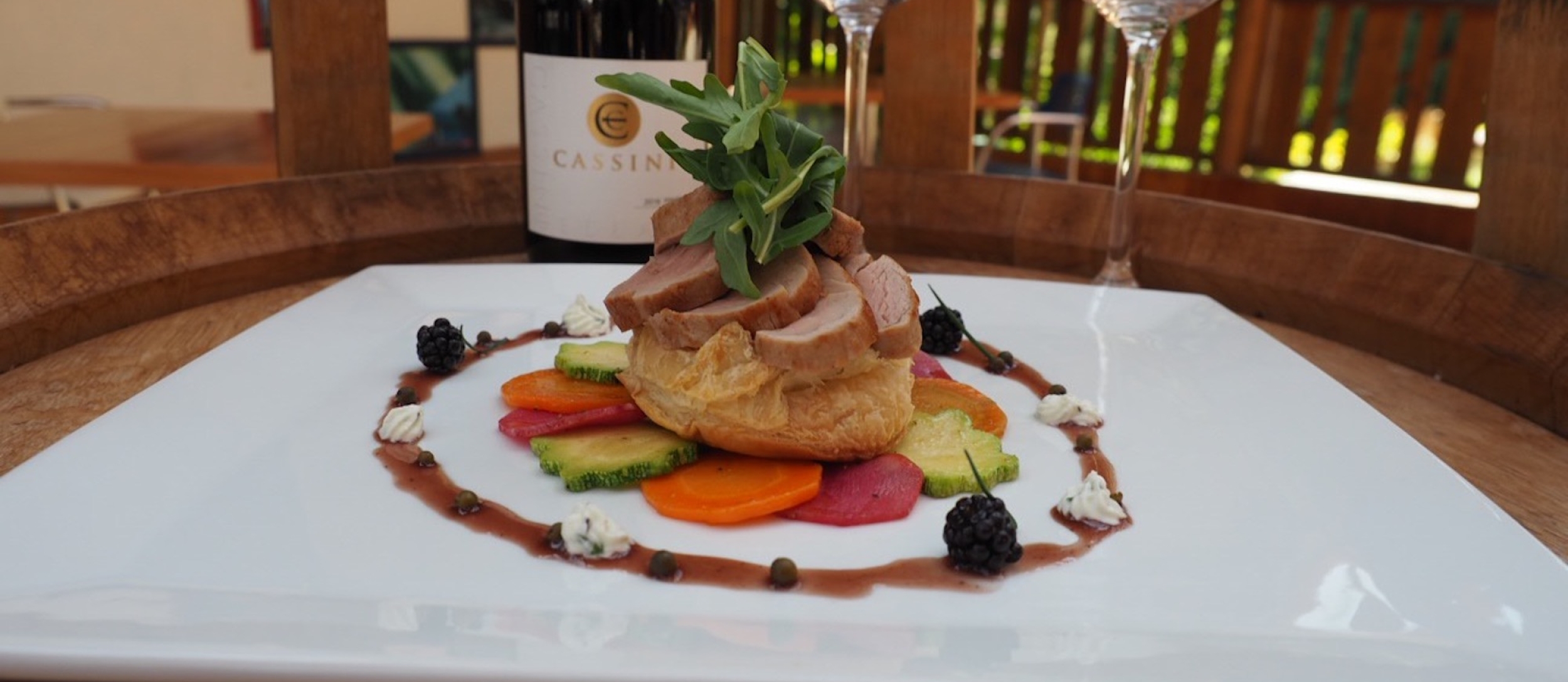 A plate of delicious looking food with two wine glasses and a bottle of red wine