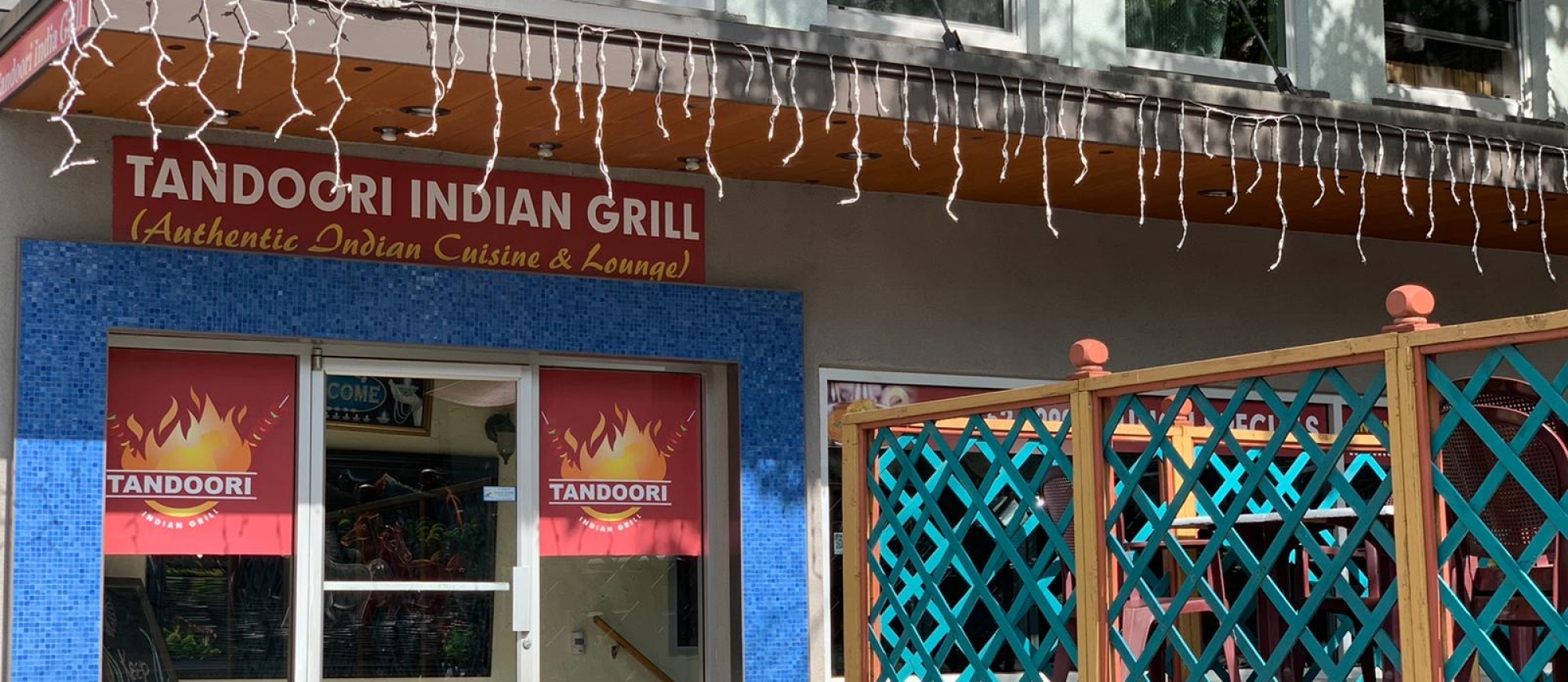 the tandoori grill building with lights hanging down and a green patio fence