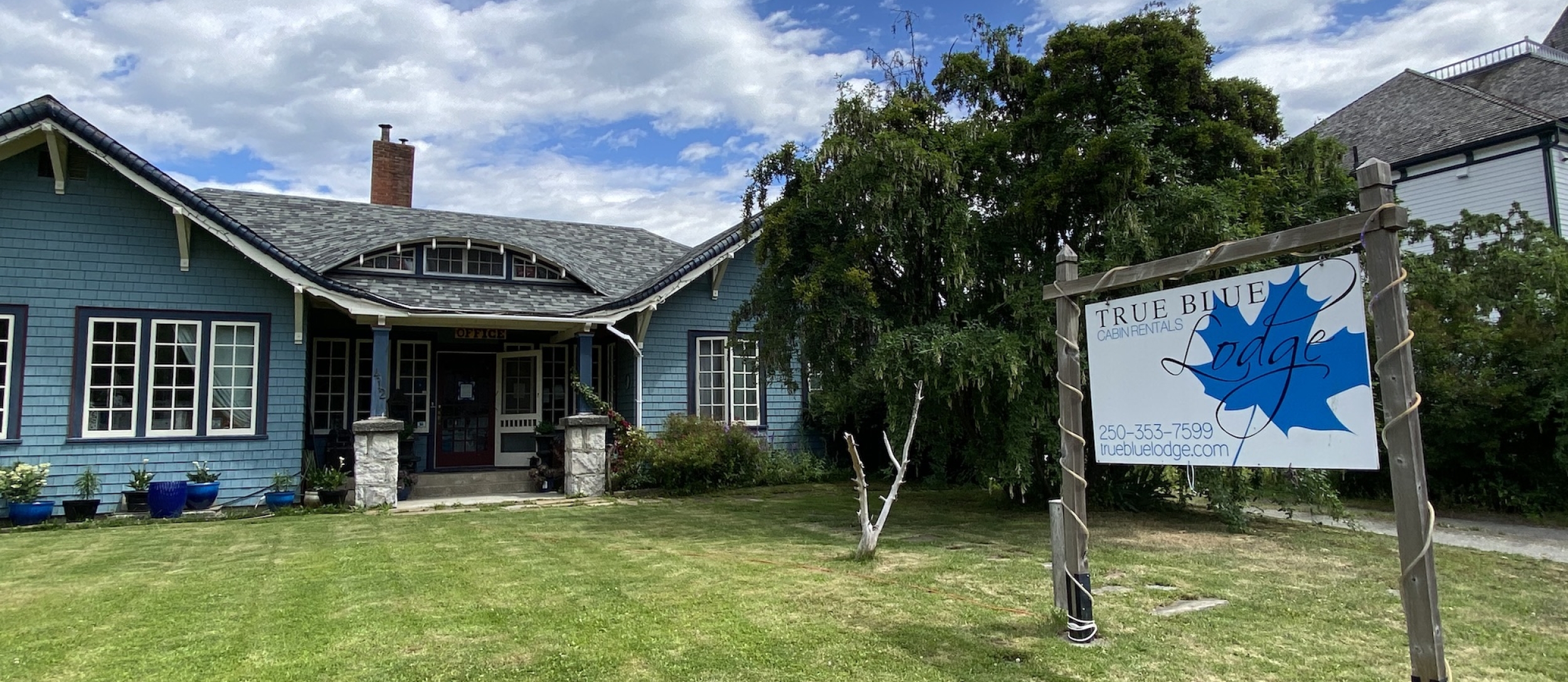 The True Blue Lodge sits in Kaslo, BC with a green yard and tall sign