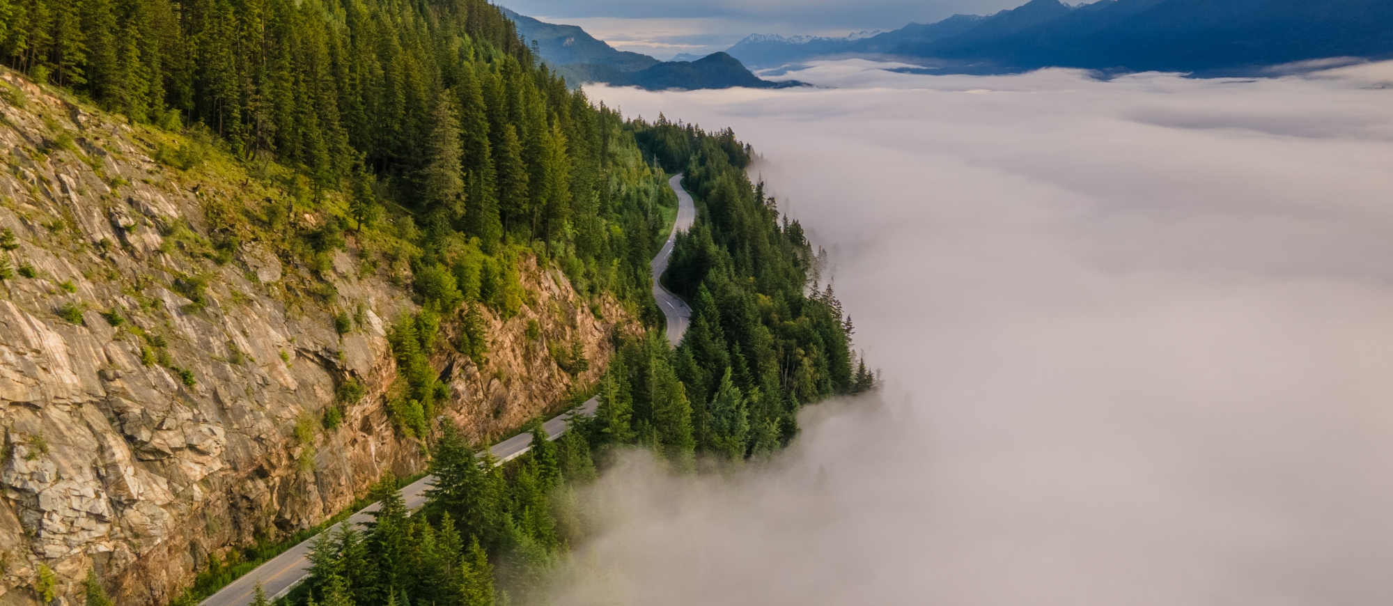 Winding highway between a foggy lake and mountains