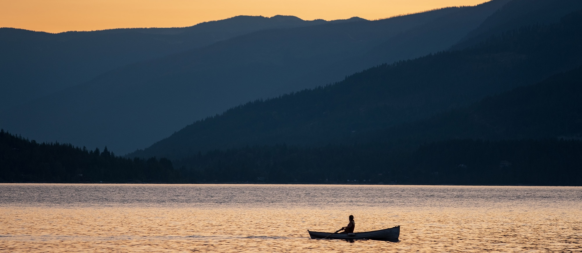 A person in a row boat silhouetted by the sunset on Kootenay Lake