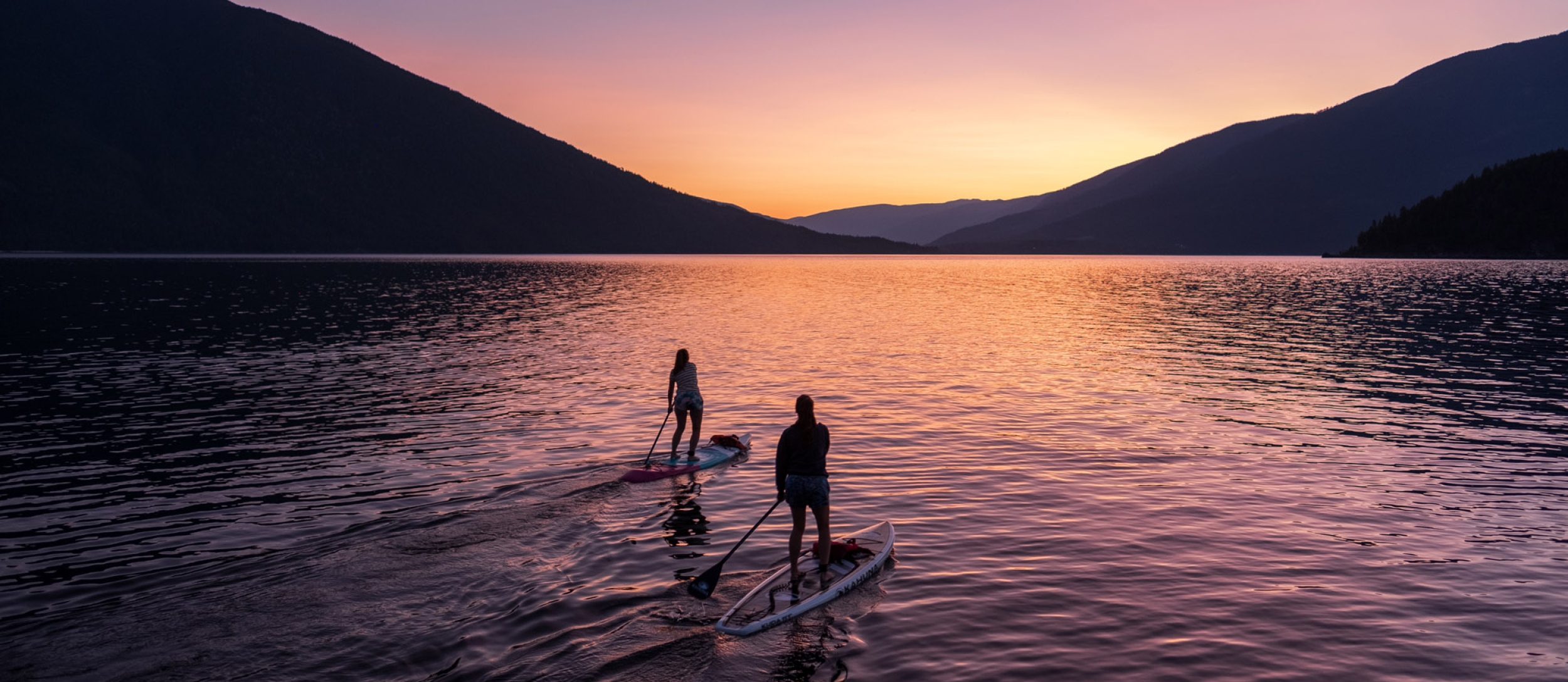 Two paddle boarders on Kootenay Lake paddling into the sunset