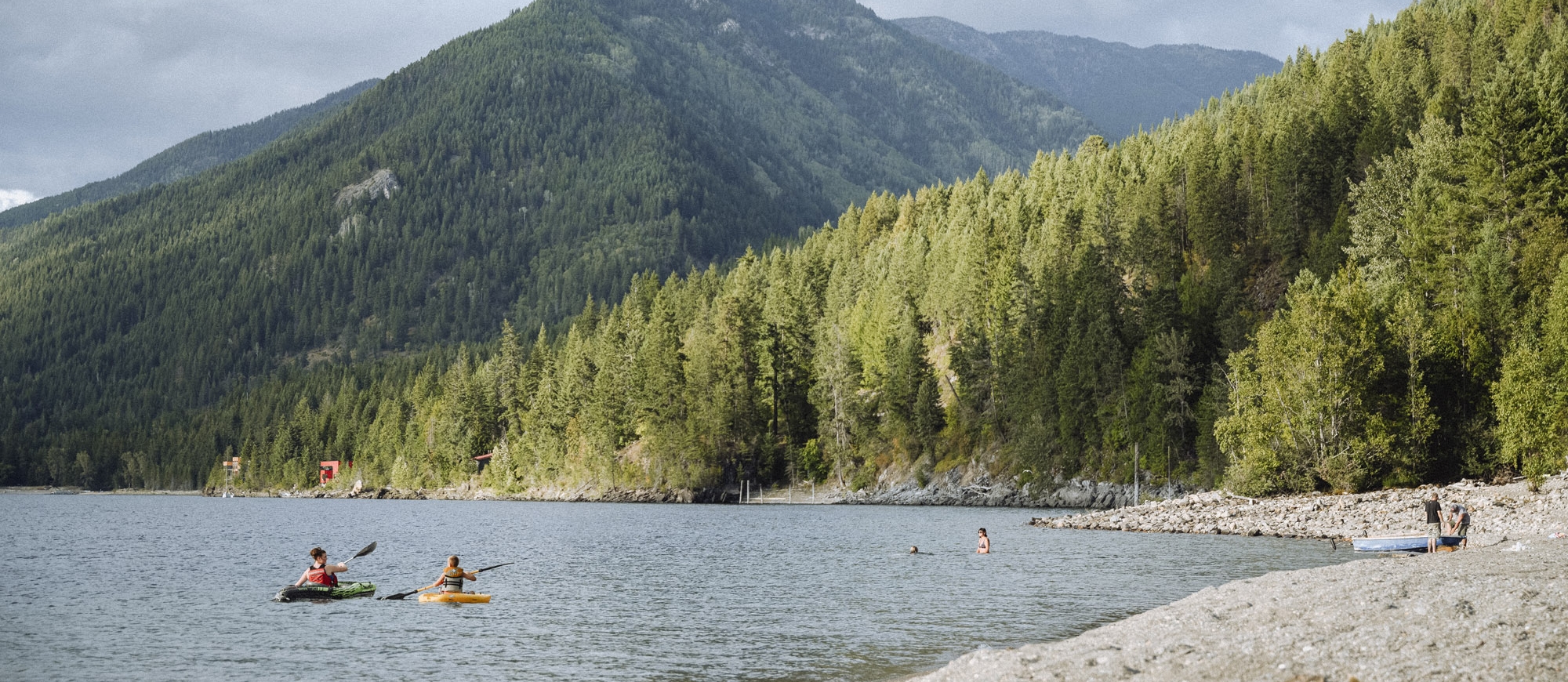 Kayakers and people on the beach with mountains in the backcountry at Lockhart Beach Provincial Park near Crawford Bay, BC