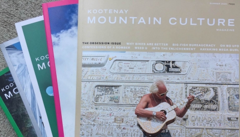 a fresh stack of Kootenay Culture Magazines. On the cover, a man plays guitar.