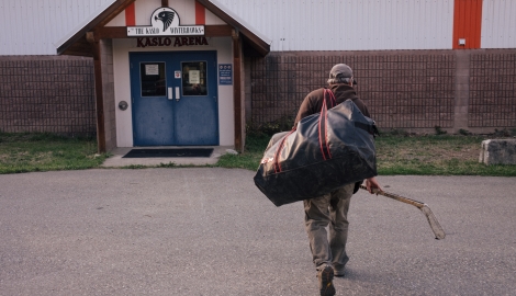 Man walking into Kaslo Arena holding a hockey stick and duffle bag