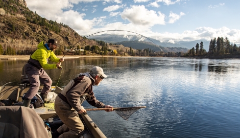 A man has a fish on his line, the other man has a net ready for him on the Columbia River with Reel Adventures