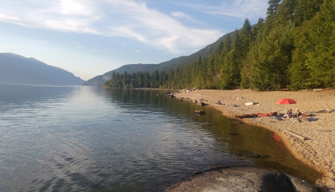 People sitting on a beach with a red sun umbrella at Barnard Beach near Riondel BC