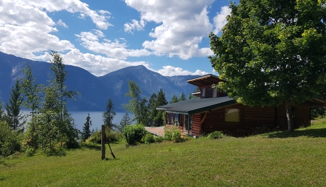 A wood cottage with a green lawn and lake view.