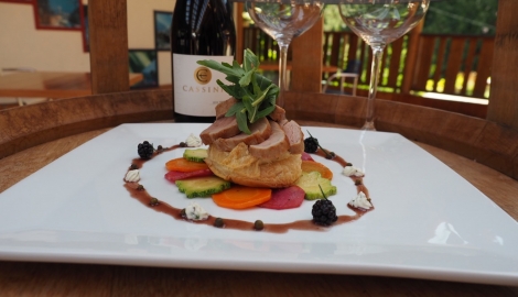 A plate of delicious looking food with two wine glasses and a bottle of red wine