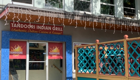 the tandoori grill building with lights hanging down and a green patio fence