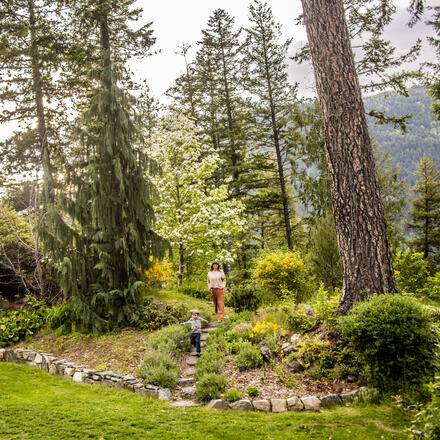 A mother and her toddler son, walking through a park with flowers blooming in Nelson BC's Gyro Park.