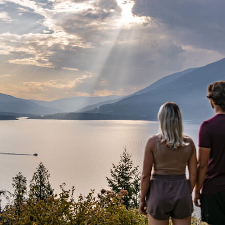 A couple looking out over Kootenay Lake with a ferry riding along the water.